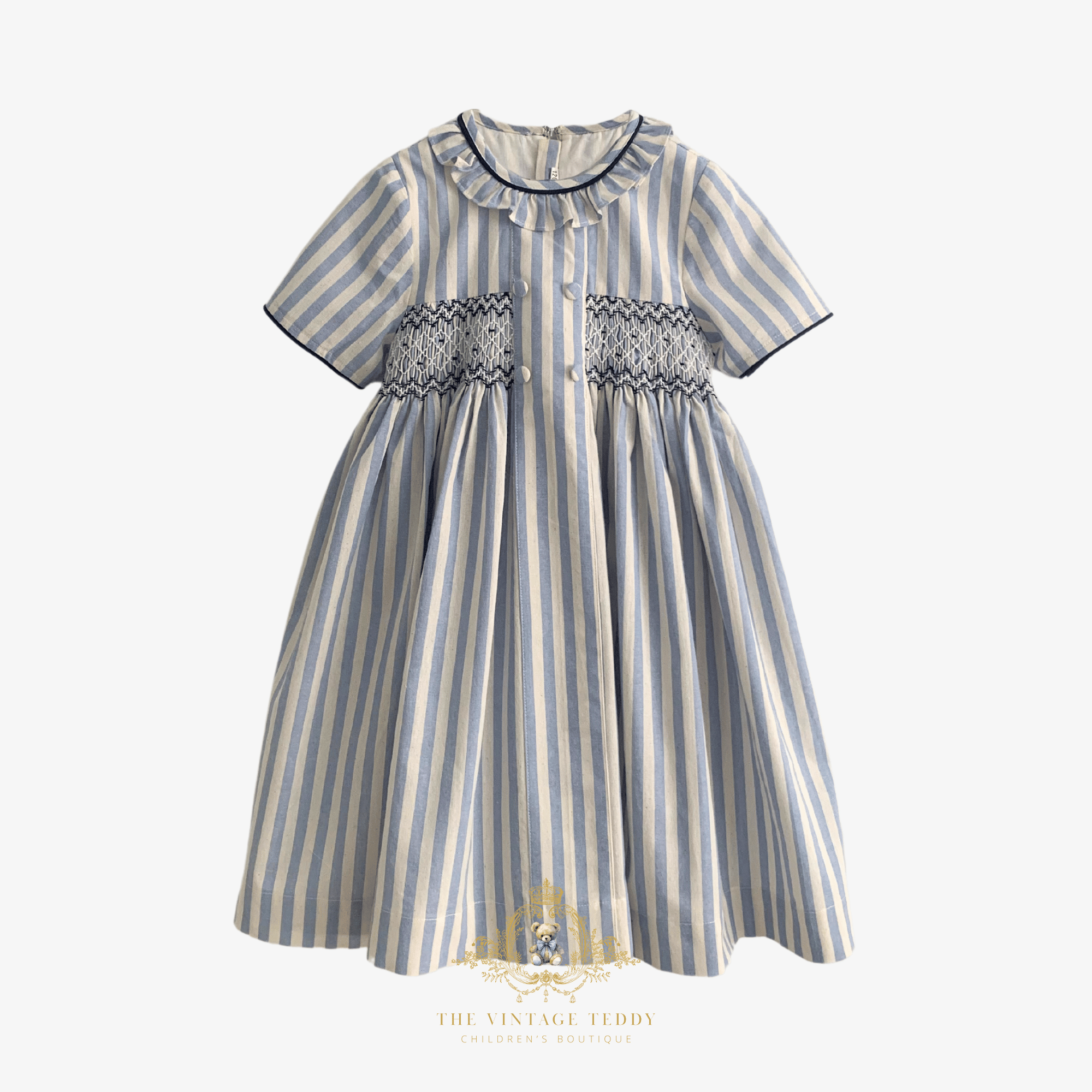 A short-sleeve baby girls dress with vertical blue and cream stripes, featuring a smocked bodice and a ruffled collar. The dress is displayed flat against a light background with a The Vintage Teddy brand watermark at the bottom.